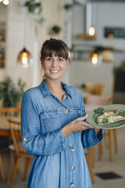 Sorridente donna d'affari in possesso di piatto di cibo mentre in piedi in caffè — Foto stock