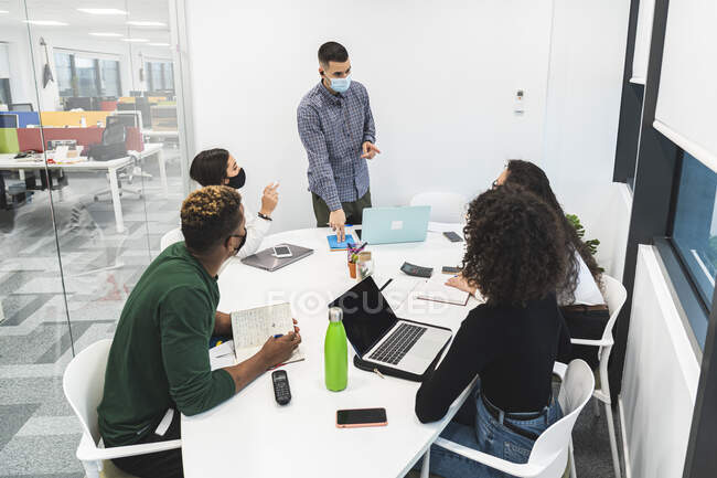 Kreativer Geschäftsmann erklärt Mitarbeitern im Sitzungssaal im Büro während COVID-19 die Geschäftsstrategie — Stockfoto