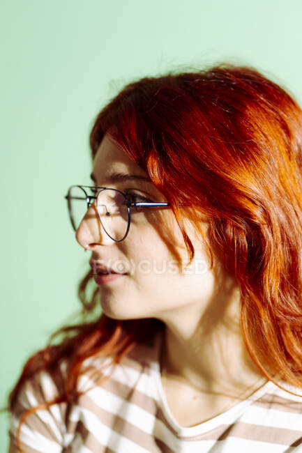Junge Frau mit Brille schaut vor grünem Hintergrund weg — Stockfoto