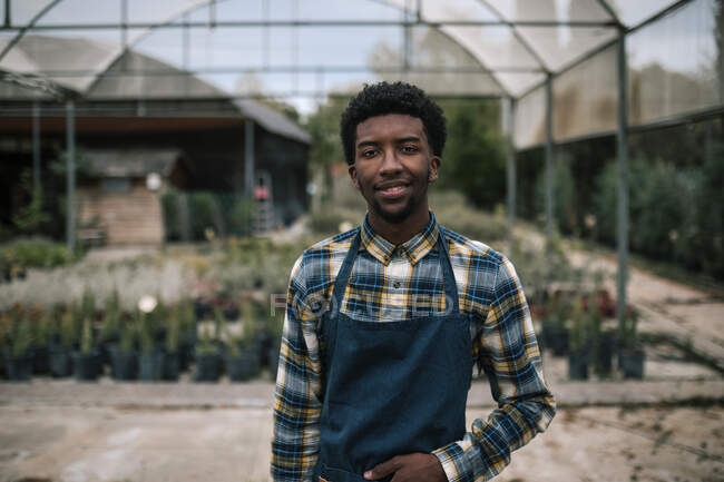 Улыбающийся молодой работник фермы, стоящий против теплицы — стоковое фото