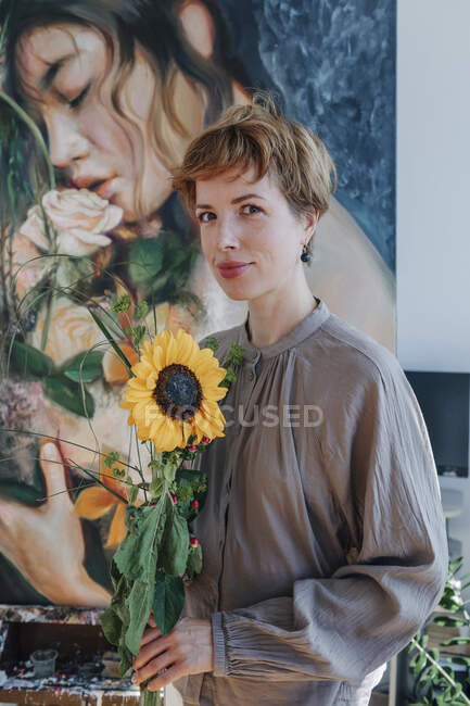 Улыбающаяся художница держит подсолнух, противостоя искусству — стоковое фото