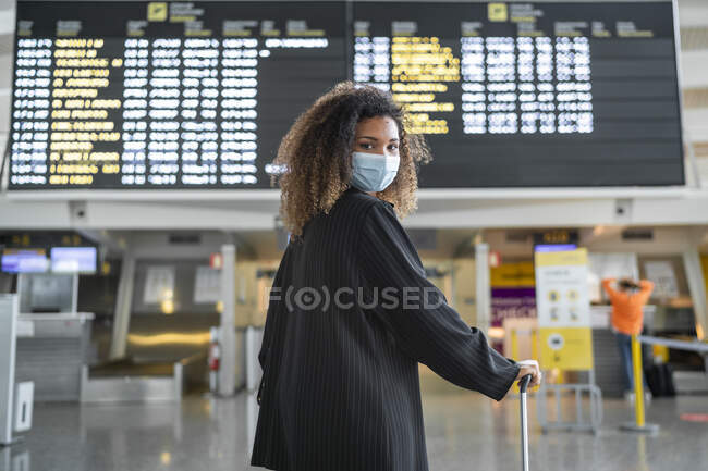 Femme portant un masque protecteur regardant par-dessus l'épaule tout en se tenant à l'aéroport — Photo de stock