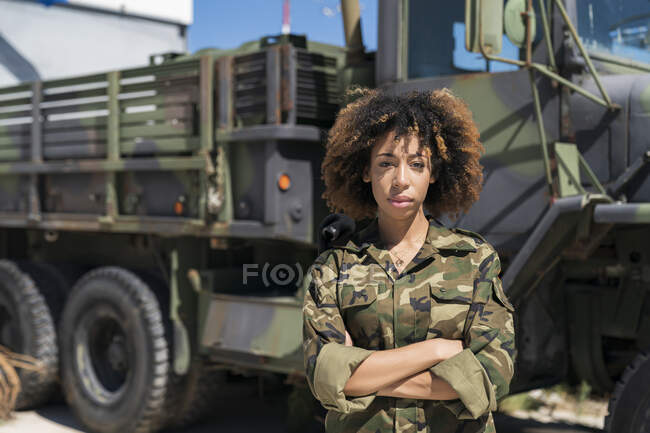 Jeune soldat militaire confiante, les bras croisés contre un camion à la base, par une journée ensoleillée — Photo de stock
