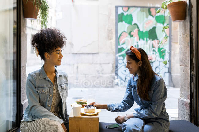Amis manger et boire tout en étant assis près de la fenêtre au café — Photo de stock