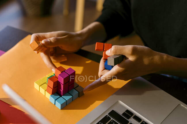 Manos de mujer de negocios jugando con bloques de juguetes por computadora portátil en casa - foto de stock
