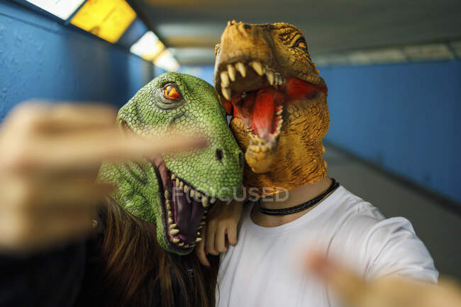 Amigos hombres y mujeres mostrando el dedo medio mientras usan máscara de dinosaurio en el pasillo - foto de stock