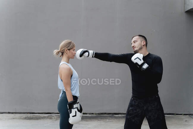 Sportsman teaching boxing to woman while standing against wall — Stock Photo
