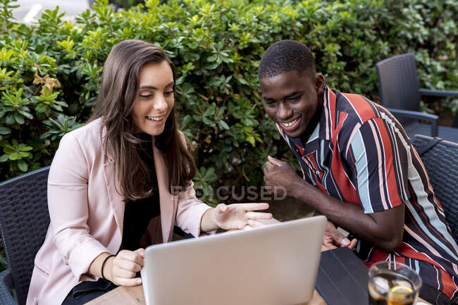 Smiling young couple looking at laptop while sitting at table in cafe — Stock Photo