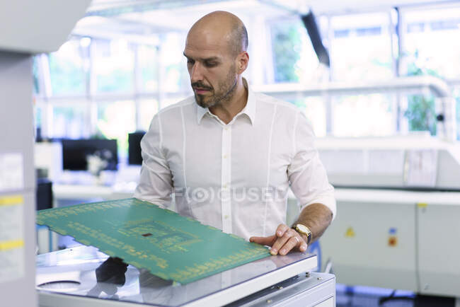 Técnico masculino maduro seguro que examina la placa de circuito grande en la fábrica - foto de stock