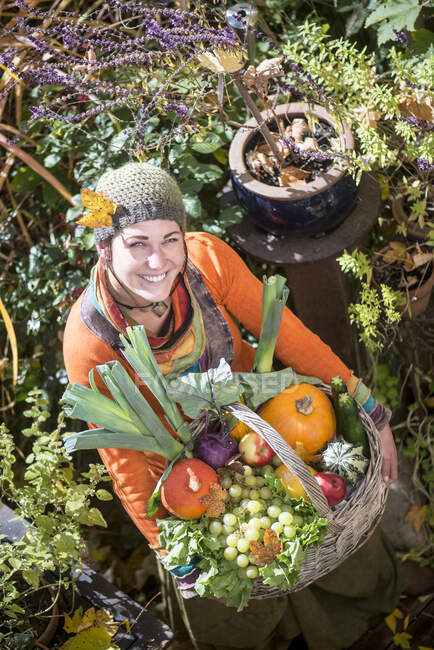 Lächelnde Frau mit Obst- und Gemüsekorb im Garten — Stockfoto