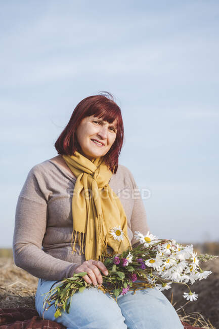 Donna anziana seduta su balla di fieno mentre tiene fiori di camomilla — Foto stock