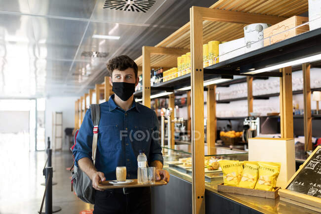 Businessman in protective face mask holding tray of drinks in cafe during COVID-19 — Stock Photo