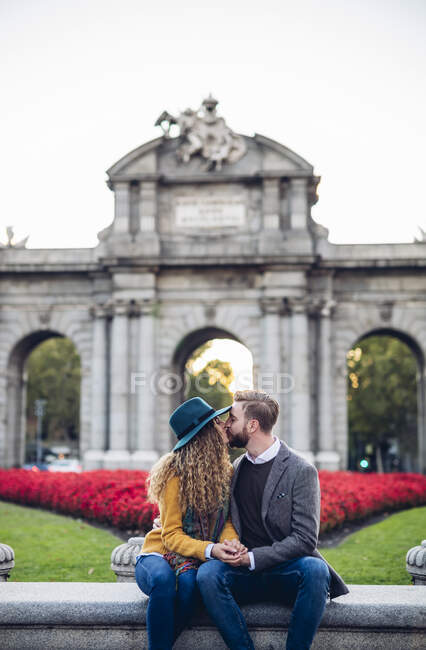 Man and woman kissing while sitting against gate in city — Foto stock