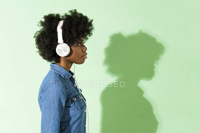 Giovane donna che indossa cuffie guardando altrove mentre in piedi sullo sfondo verde — Foto stock