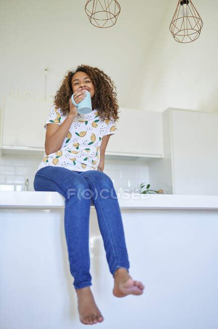 Mujer joven sonriente con taza de café en el mostrador de la cocina en casa - foto de stock