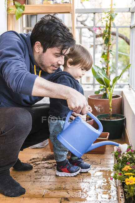 Uomo e ragazzo irrigazione pianta insieme mentre in piedi al balcone — Foto stock
