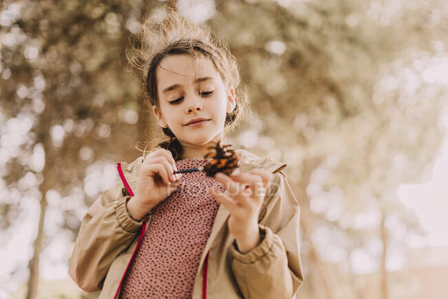 Cute girl coloring pine cone with paintbrush at park — Stock Photo