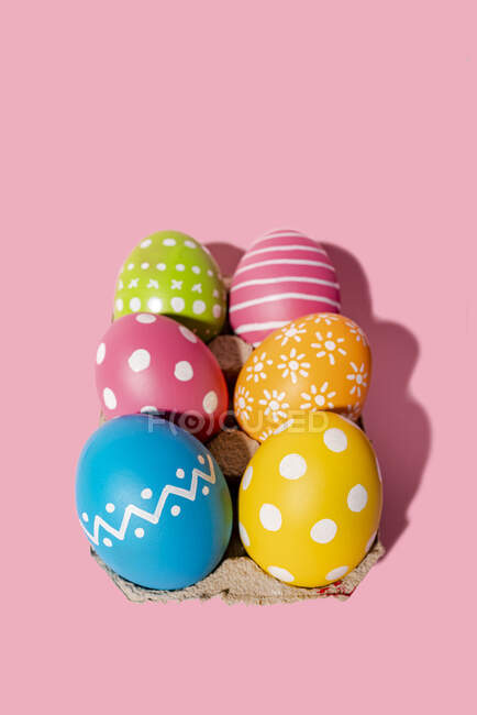 Variation of design and hand colored Easter eggs in tray on pink background — Stock Photo