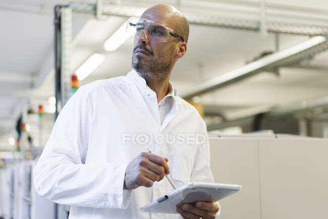 Maturo tecnico maschio in possesso di tablet digitale mentre guardando lontano in laboratorio — Foto stock