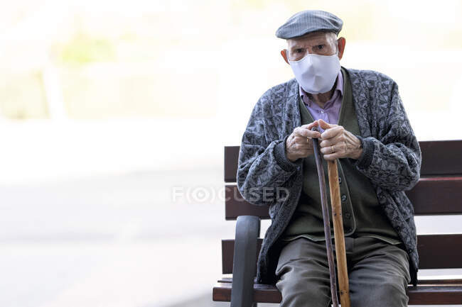 Uomo anziano con maschera protettiva seduta sulla panchina all'aperto — Foto stock