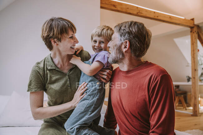Счастливая мать обнимает сына, в то время как отец сидит рядом с кроватью дома — стоковое фото