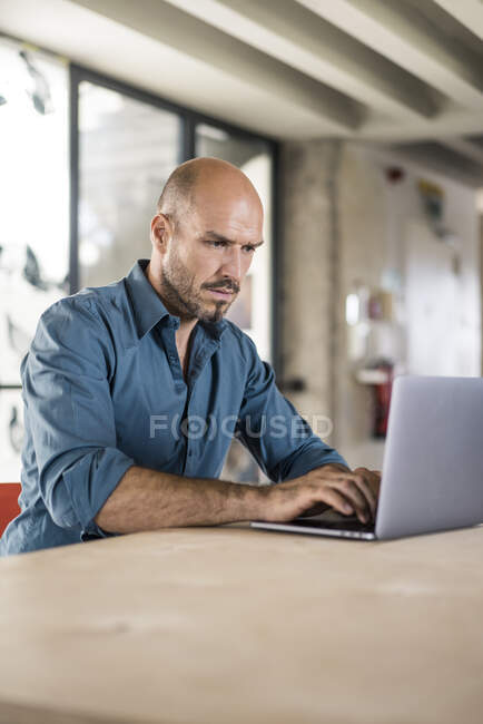 Empresario trabajando en el ordenador portátil mientras está sentado junto a la mesa en la oficina - foto de stock