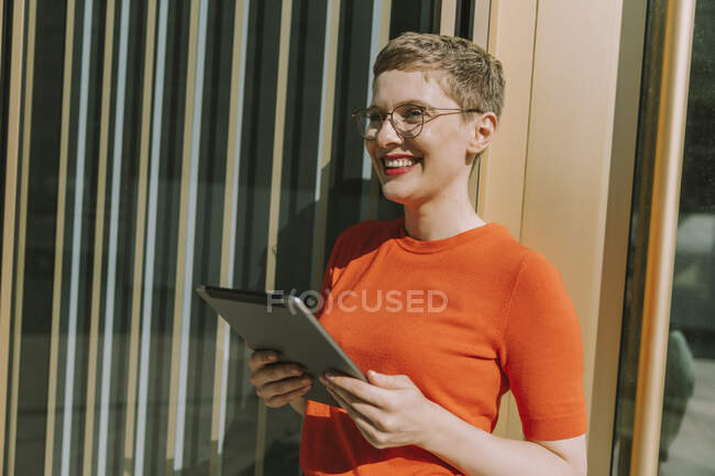 Donna sorridente utilizzando tablet digitale mentre in piedi nella giornata di sole — Foto stock