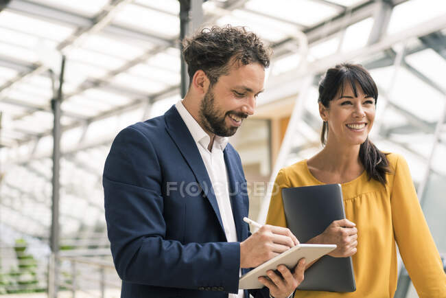 Sorridente collega maschio utilizzando tablet digitale in piedi da imprenditore femminile in ufficio — Foto stock