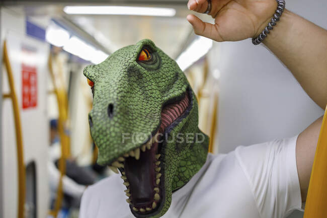 Hombre con máscara de dinosaurio mientras viaja en tren - foto de stock
