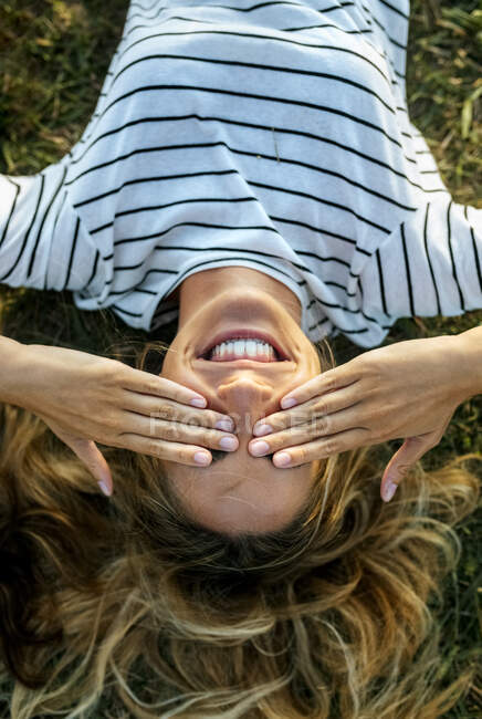 Feliz joven mujer cubriendo los ojos con las manos mientras se relaja en el campo - foto de stock