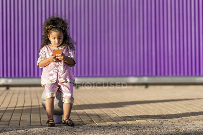 Nettes Mädchen benutzt Handy, während es gegen lila Wand sitzt — Stockfoto