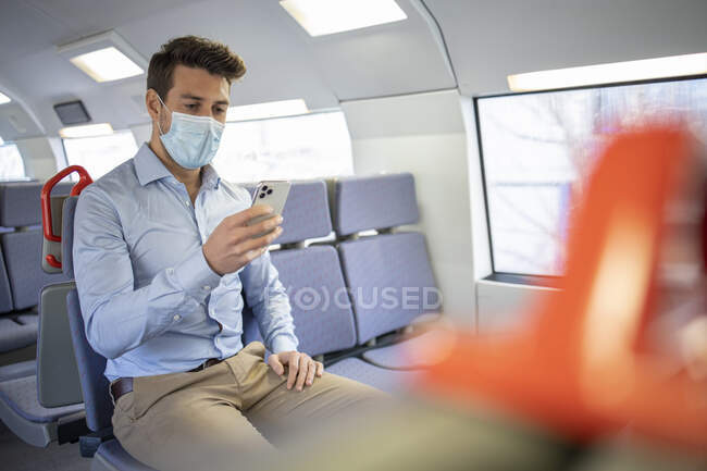 Businessman wearing protective face mask using mobile phone while sitting in train — Fotografia de Stock