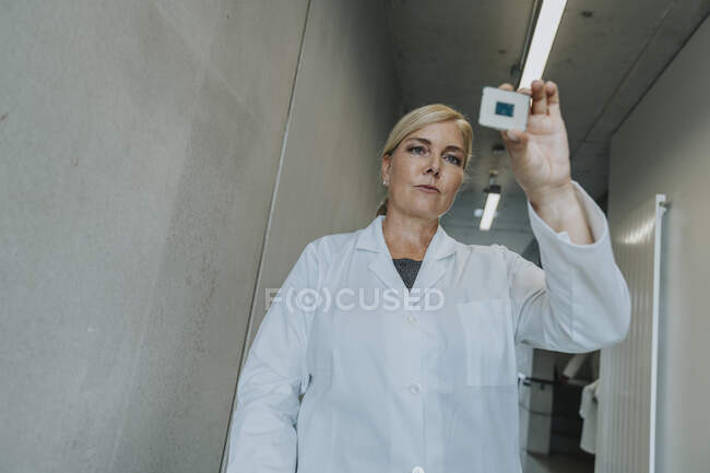 Femme blonde tenant une puce d'ordinateur tout en étant debout au couloir de la clinique — Photo de stock