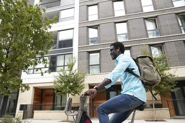 Homme souriant écoutant de la musique tout en faisant la navette à vélo en ville — Photo de stock