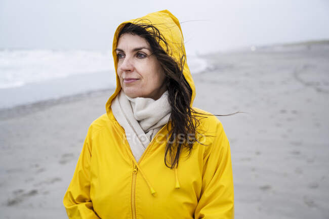 Mulher madura contemplada em capa de chuva amarela na praia durante o fim de semana — Fotografia de Stock