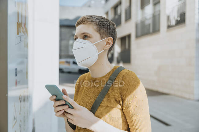 Mulher vestindo máscara protetora ler mapa enquanto segurando telefone inteligente em pé na cidade no dia ensolarado — Fotografia de Stock