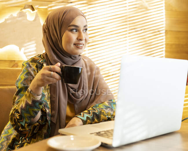 Donna che indossa hijab bere caffè mentre seduto al caffè — Foto stock