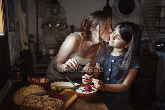 Madre baciare figlia mentre in piedi in cucina a casa — Foto stock