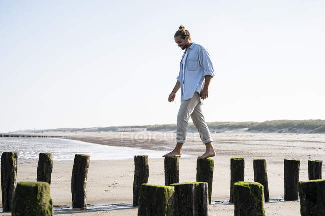 Smiling young man walking on wooden posts at beach against clear sky — Stock Photo