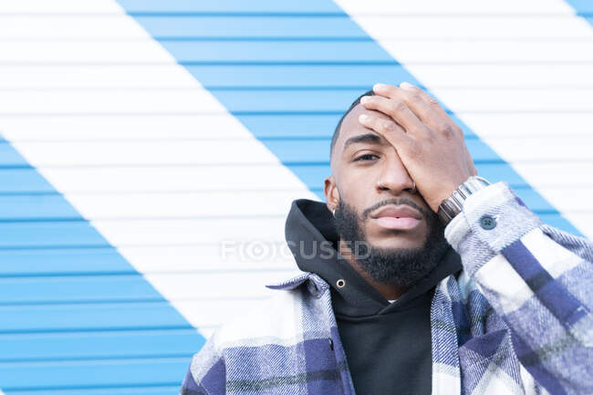 Jeune homme avec une attitude fraîche couvrant oeil contre mur ondulé — Photo de stock