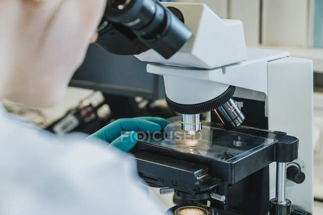 Young woman analyzing human brain microscope slide under microscope while sitting at laboratory — Stock Photo