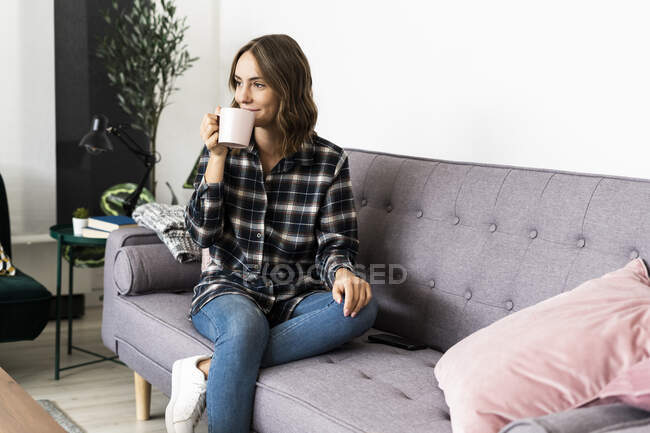 Donna che beve caffè mentre è seduta sul divano a casa — Foto stock