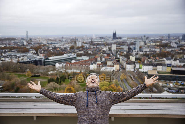 Mature man smiling while standing with arms outstretched on rooftop — Stock Photo