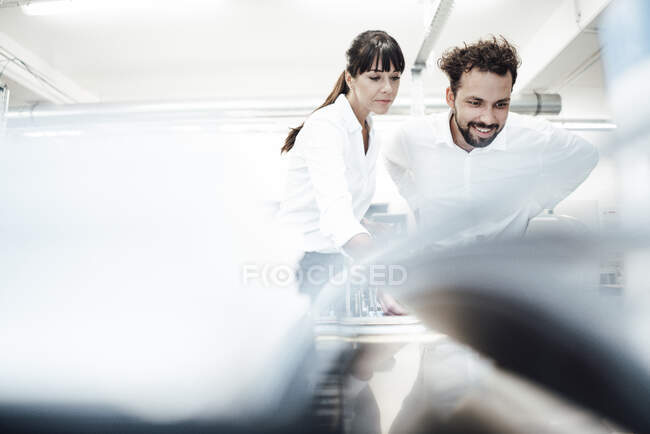 Smiling engineer by female colleague looking at machinery in industry — Stock Photo