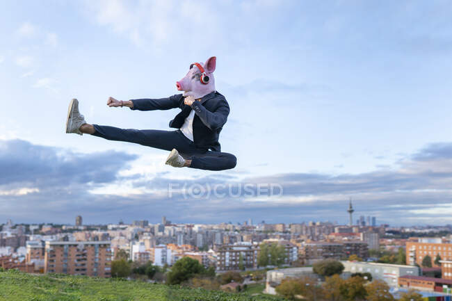 Male entrepreneur wearing pig mask practicing kickboxing while jumping against sky — Stock Photo