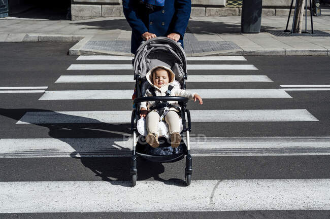 Отец с ребенком в детской коляске переходит дорогу в городе — стоковое фото