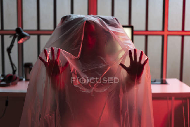 Young woman gesturing while covered with plastic at home office during COVID-19 — Stock Photo