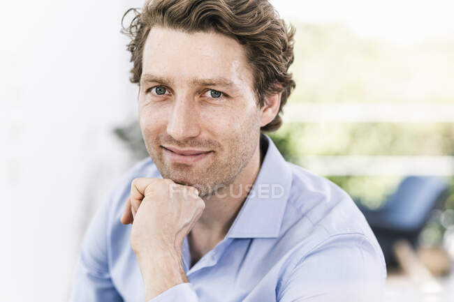 Homme souriant avec la main sur le menton assis dans le bureau — Photo de stock