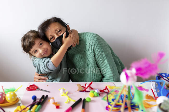 Granddaughter embracing grandmother by table against wall at home during COVID-19 — Foto stock