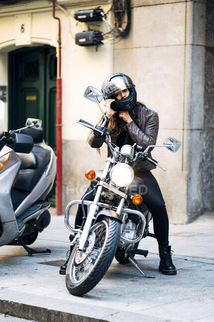 Feminino motociclista fixação acidente capacete enquanto sentado na motocicleta na calçada — Fotografia de Stock